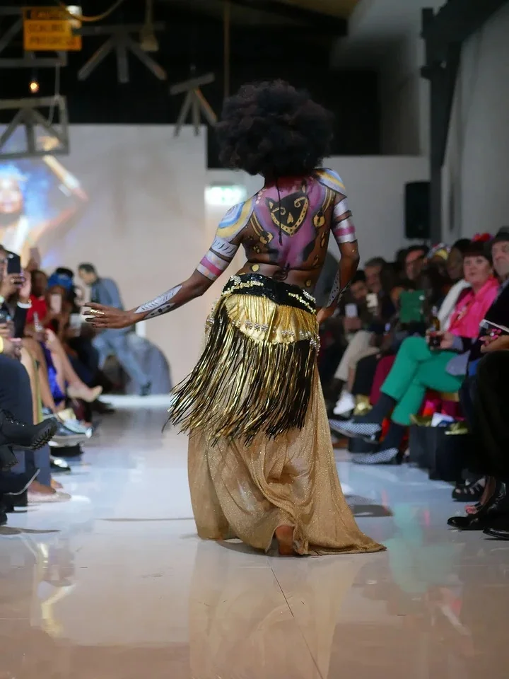 A dancer with painted back and a gold fringed skirt turns on the runway at FreekÀ 2016, the front row holding up phones